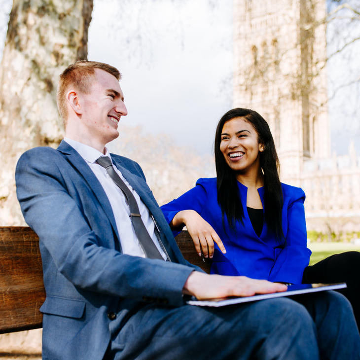 Two Hull Politics students sit smiling on a bench outside the Houses of Parliament while on placement in Westminster.