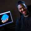 Hull Psychology student, Aaron Hall, smiling in front of a screen showing an animation of the human brain.