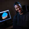 Hull Psychology student, Aaron Hall, smiling in front of a screen showing an animation of a human brain.
