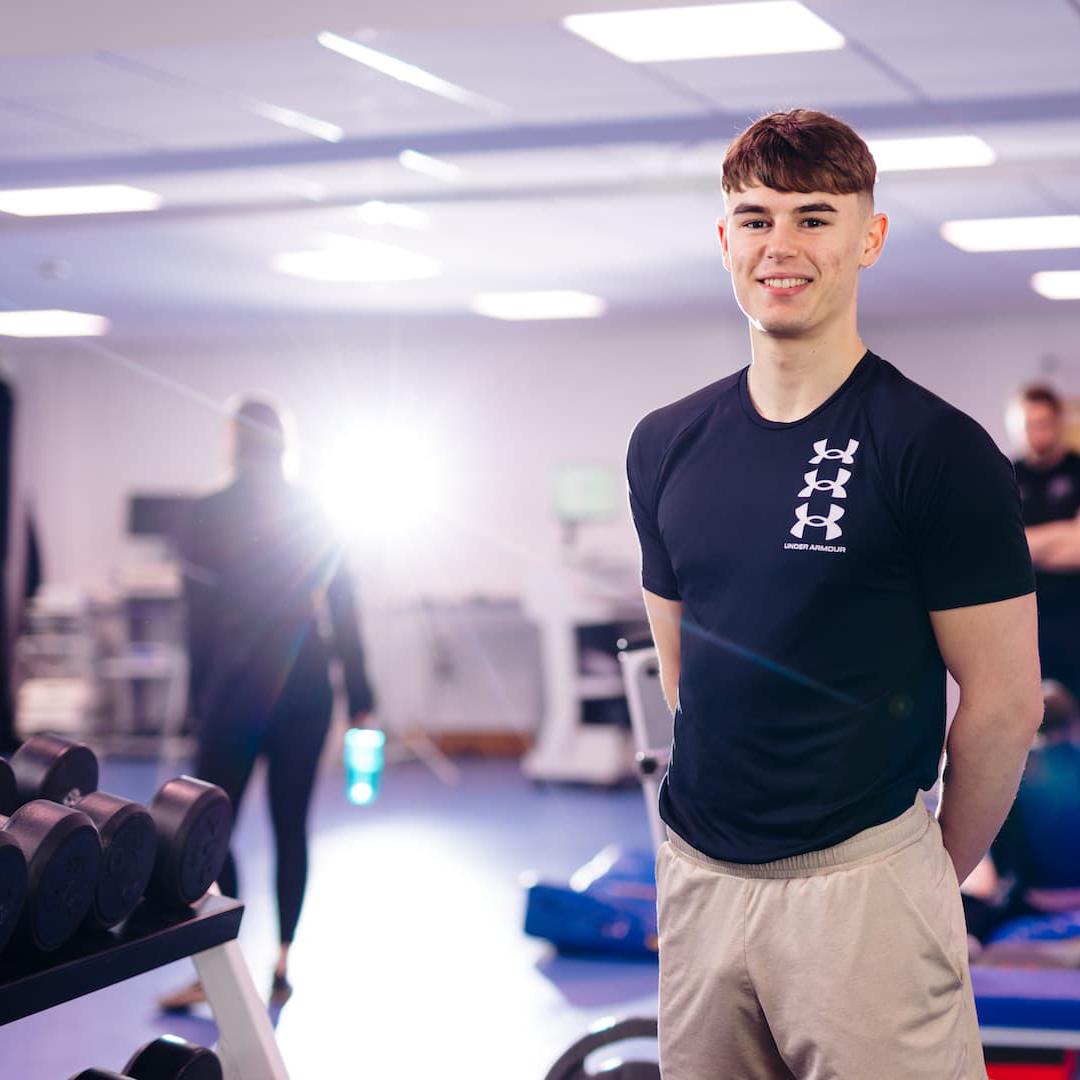 A sport student standing in a gym area with equipment behind