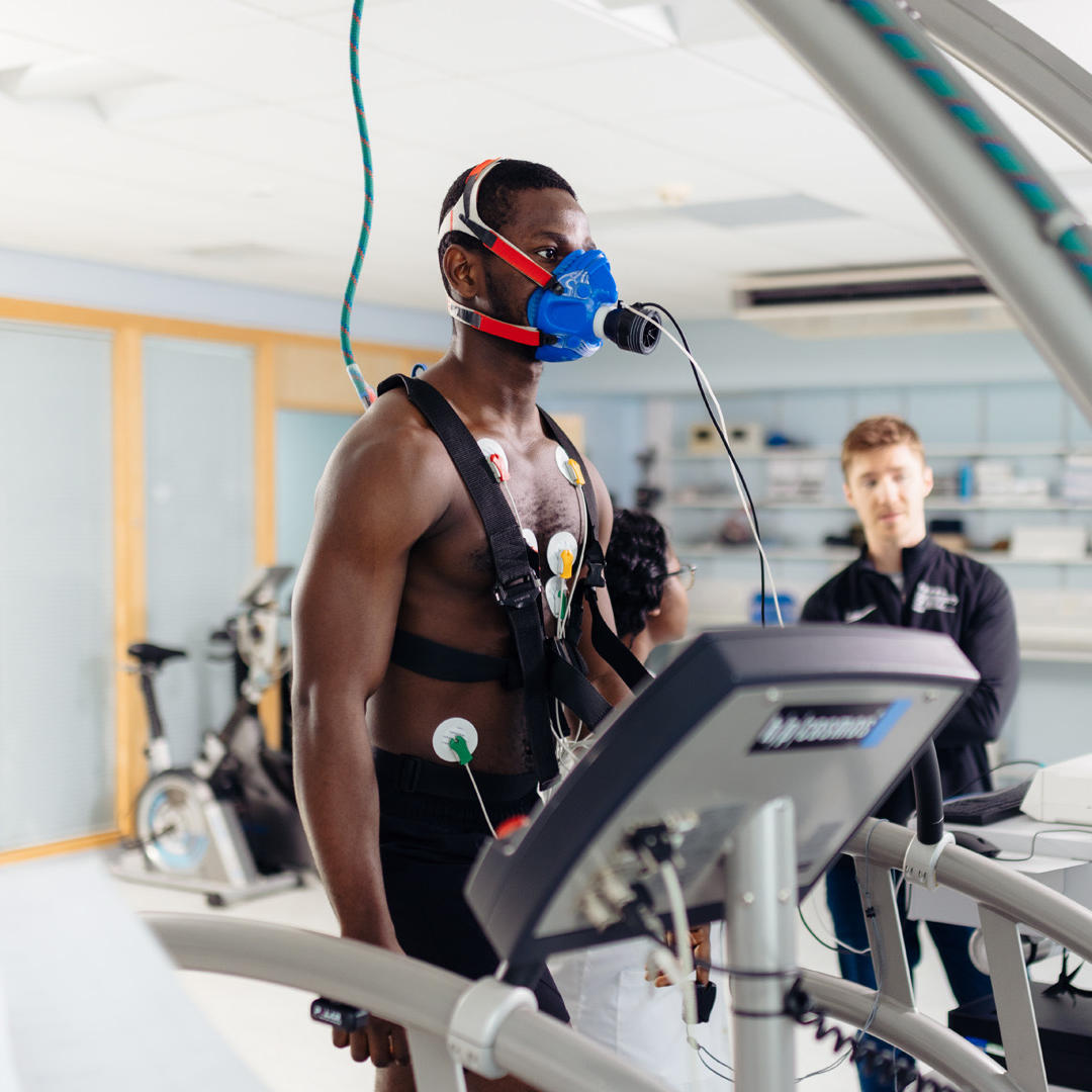A shirtless student stood on a treadmill wearing monitoring equipment