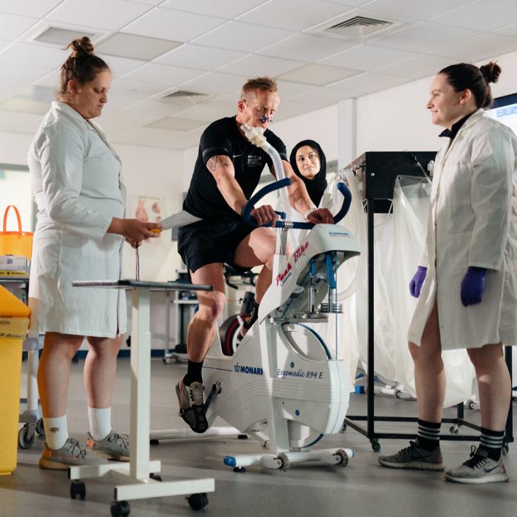 students gathered around an exercise bike gathering data in Biomechanics Lab