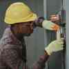 An electrician in a hard hat and protective gloves working on a home circuit