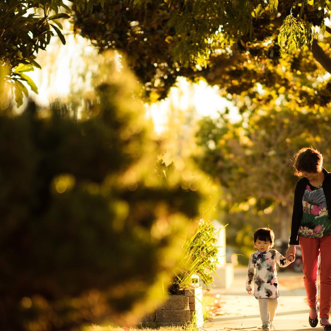 A mother and daughter taking a walk down a path in a leafy suburb