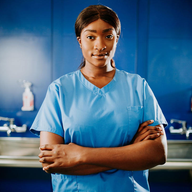 ODP student Olayemi Ajayi stands in scrubs with her arms folded in front of the hand washing station