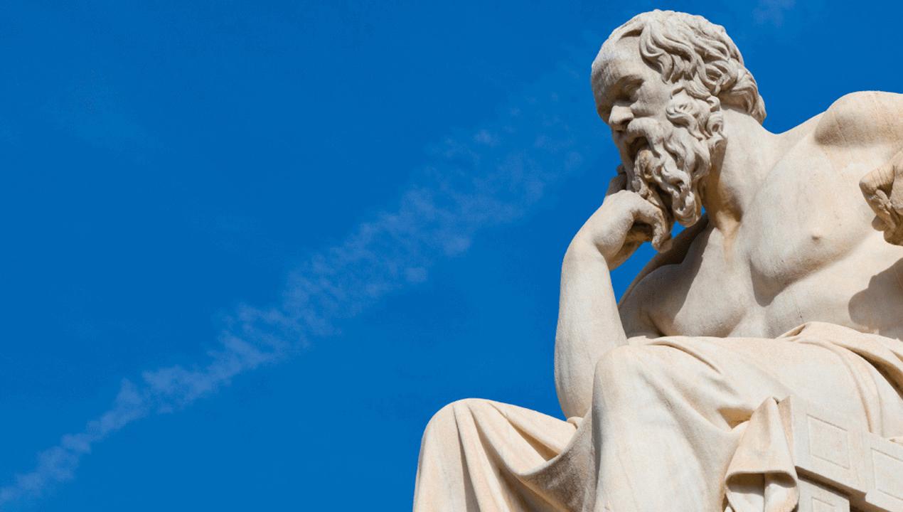 Statue of ancient Greek philosopher, Plato. He sits in a chair, hand under his chin, in an expression of deep thinking.