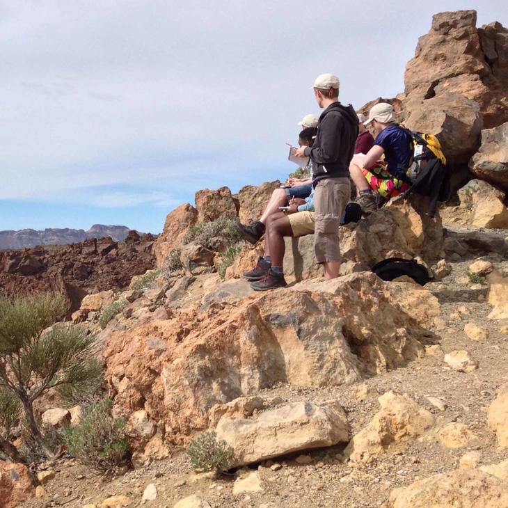 A group of Hull students sit on the rocks taking notes while on a field trip in Tenerife.