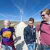 Three students walk down a path surrounded by wind turbines