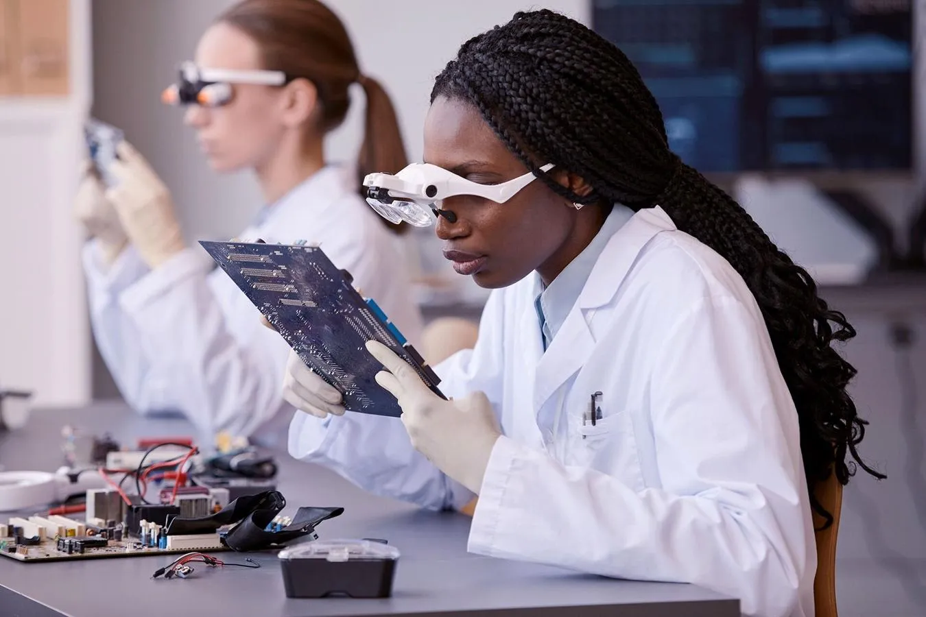 Portrait of young black woman wearing magnifying glasses and inspecting electronic circuit board in quality control lab