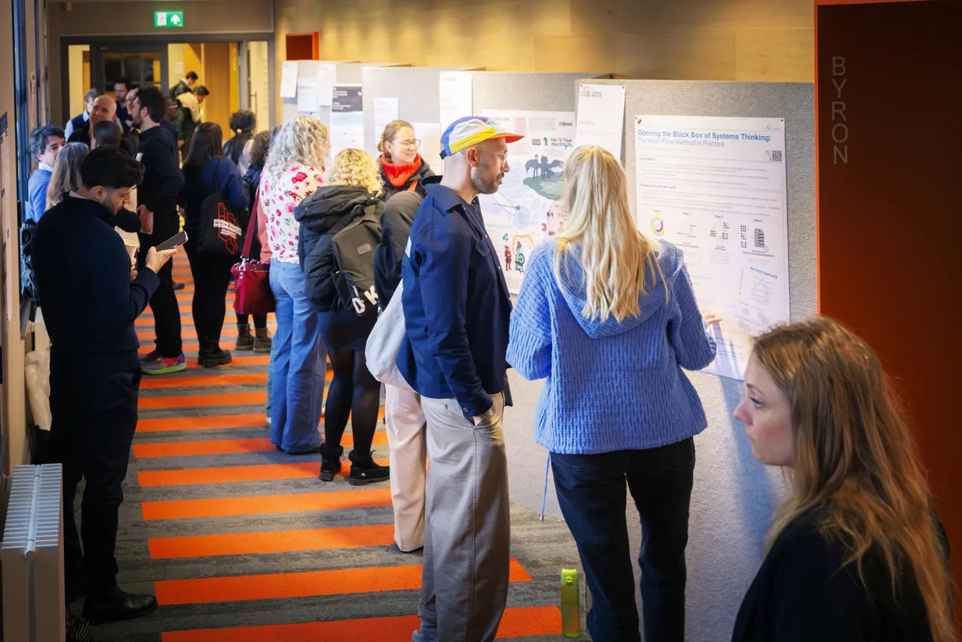 People standing in a hallway viewing and discussing posters or presentations displayed on the wall.