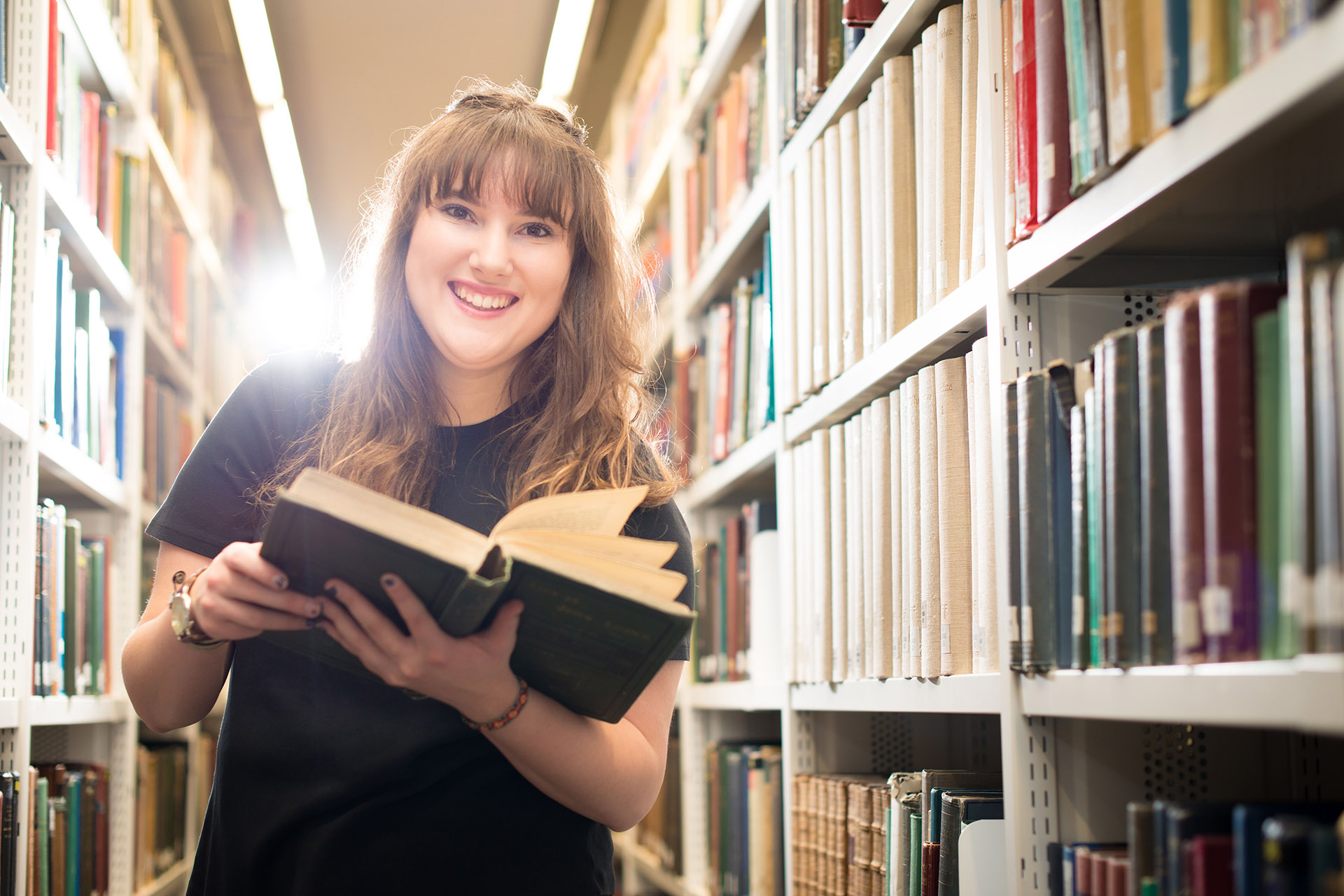 Student in Brynmor Jones Library holding a book and smiling at camera