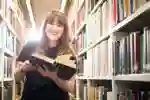 Student in Brynmor Jones Library holding a book and smiling at camera
