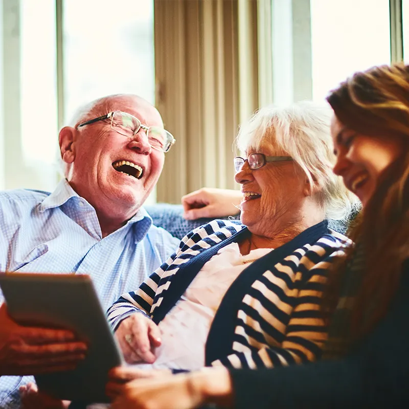 Two older adults and a younger adulat laughing looking at an ipad