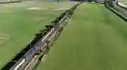 Aerial view of a freight train traveling through green fields next to a road 