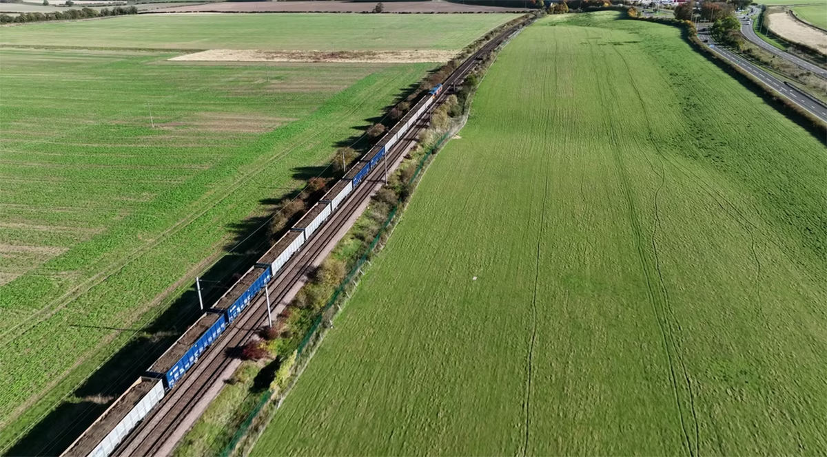 Aerial view of a freight train traveling through green fields next to a road 