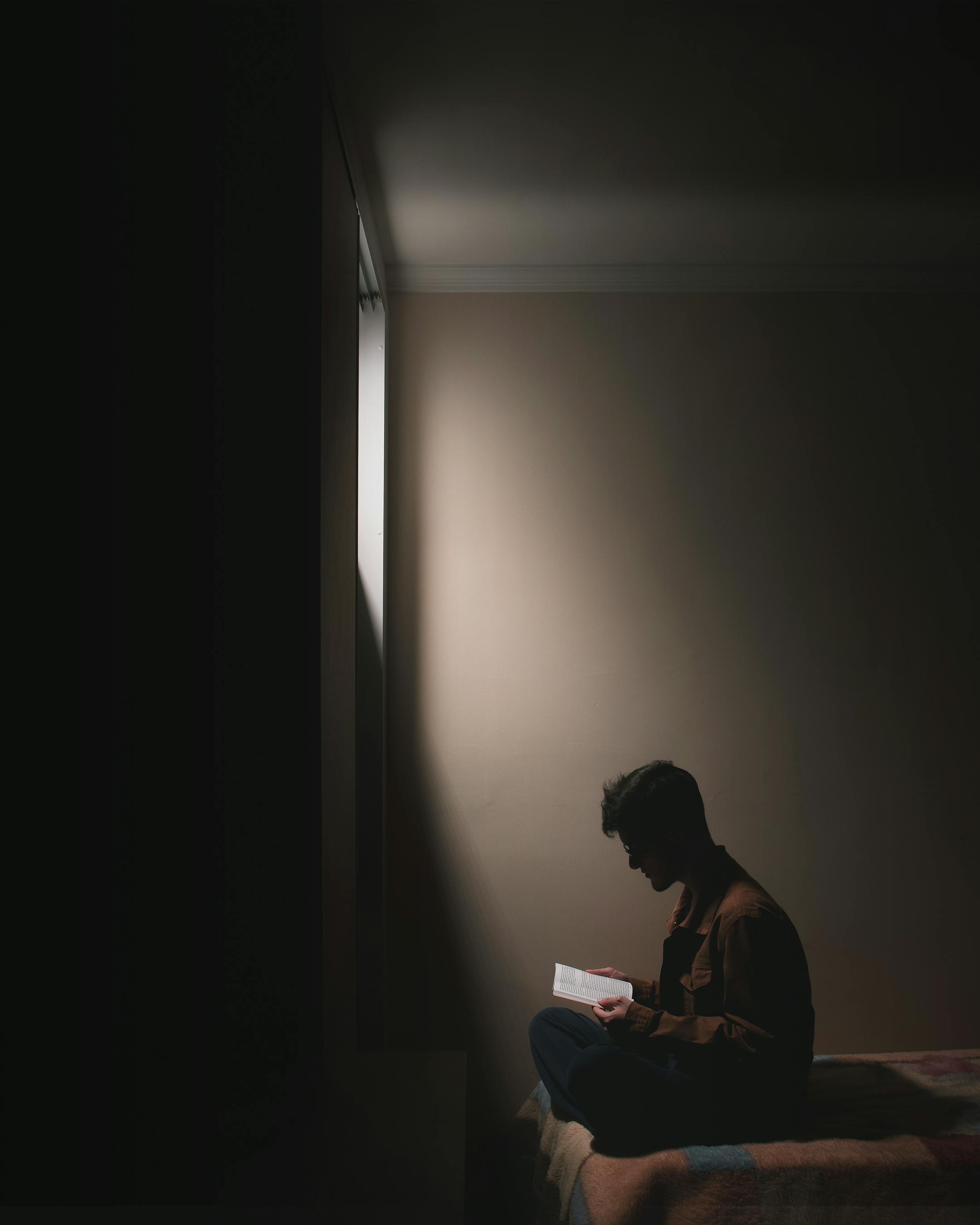 A silhouetted figure sits on a bed reading