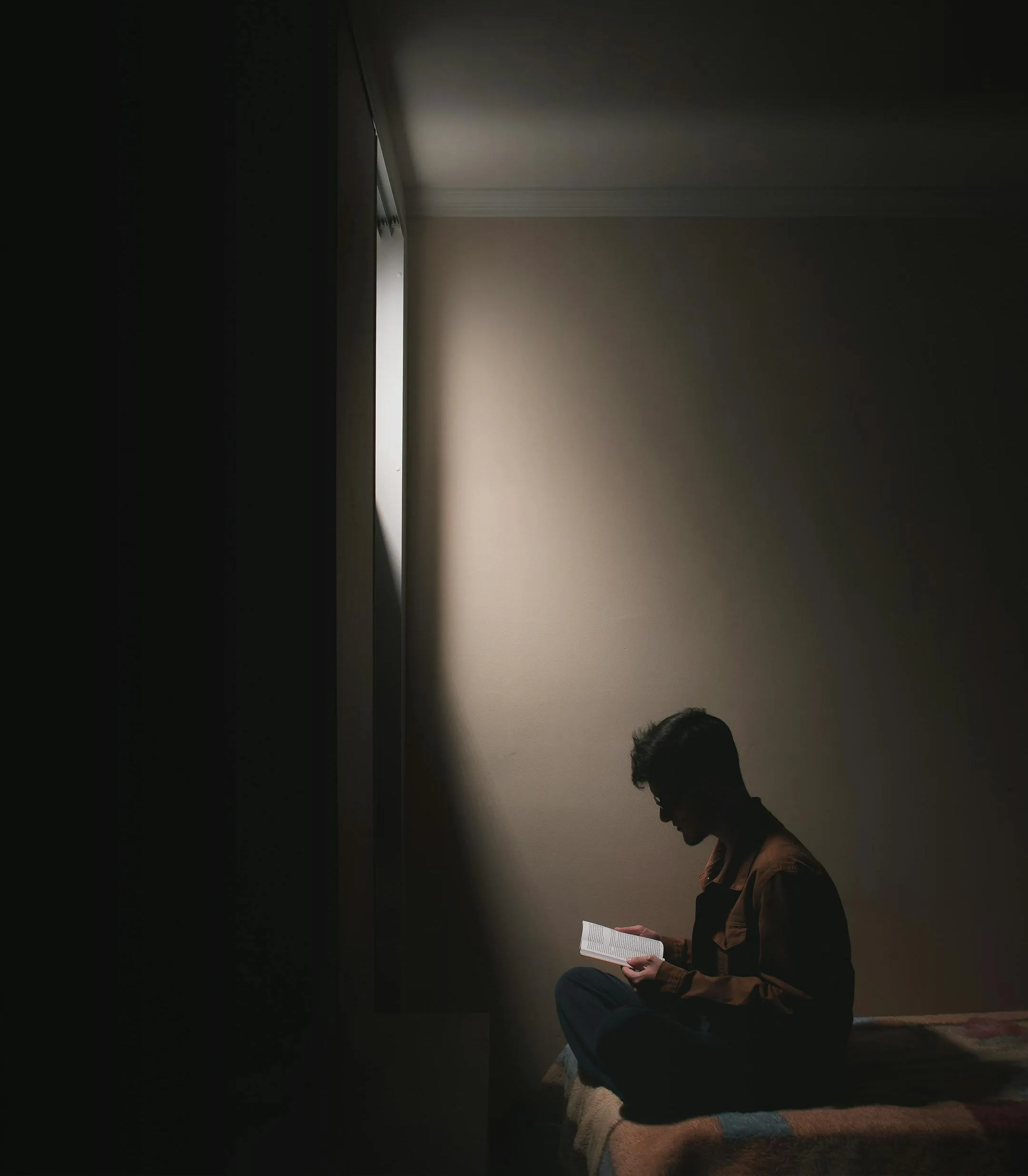 A silhouetted figure sits on a bed reading