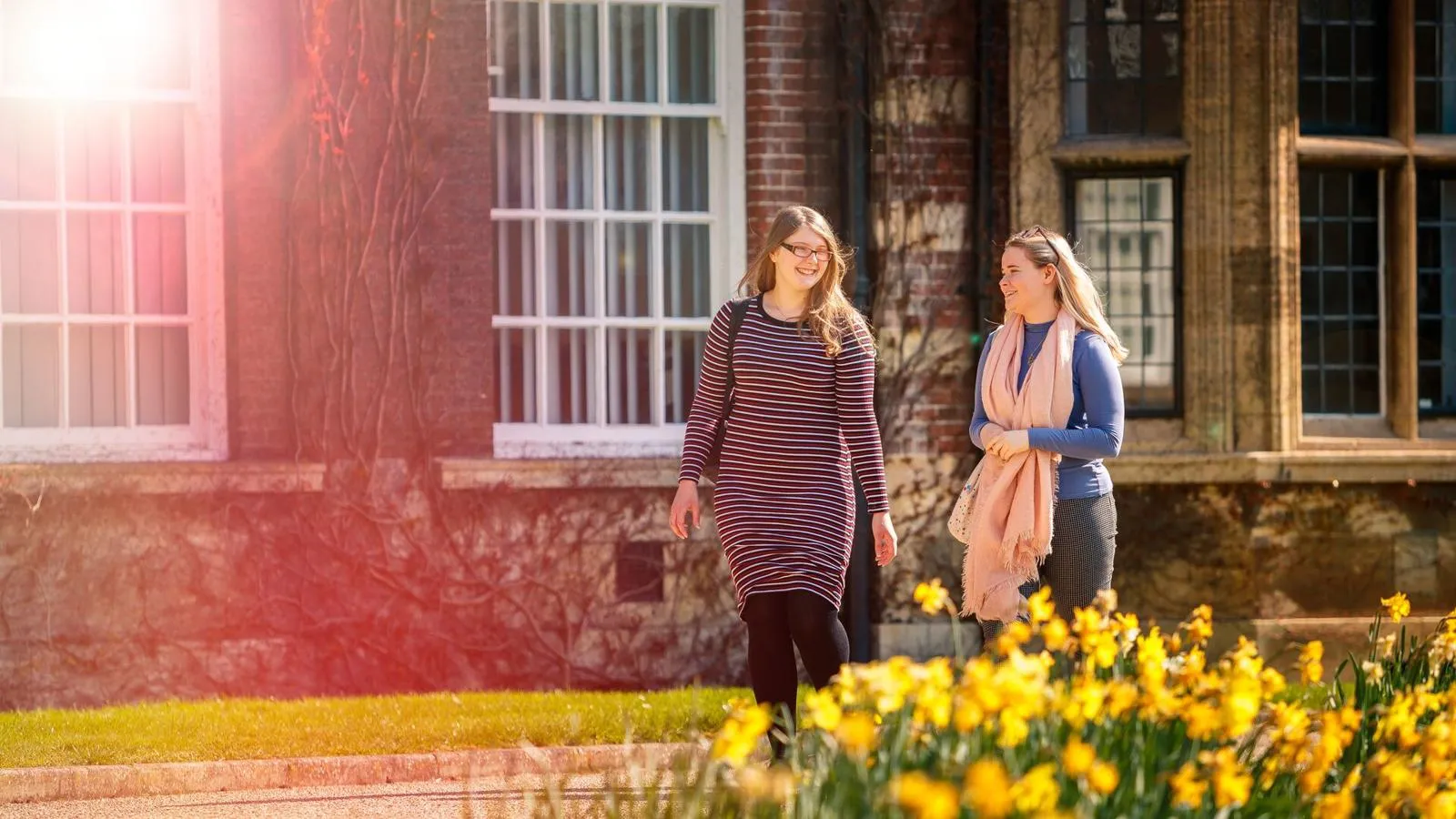Two students walking through Hull University Business school gardens on a sunny day.