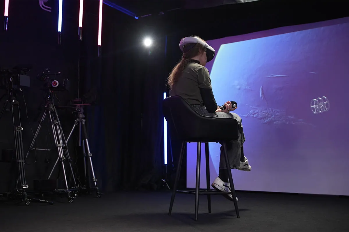 A student wearing a VR headset sits in front of a screen 
