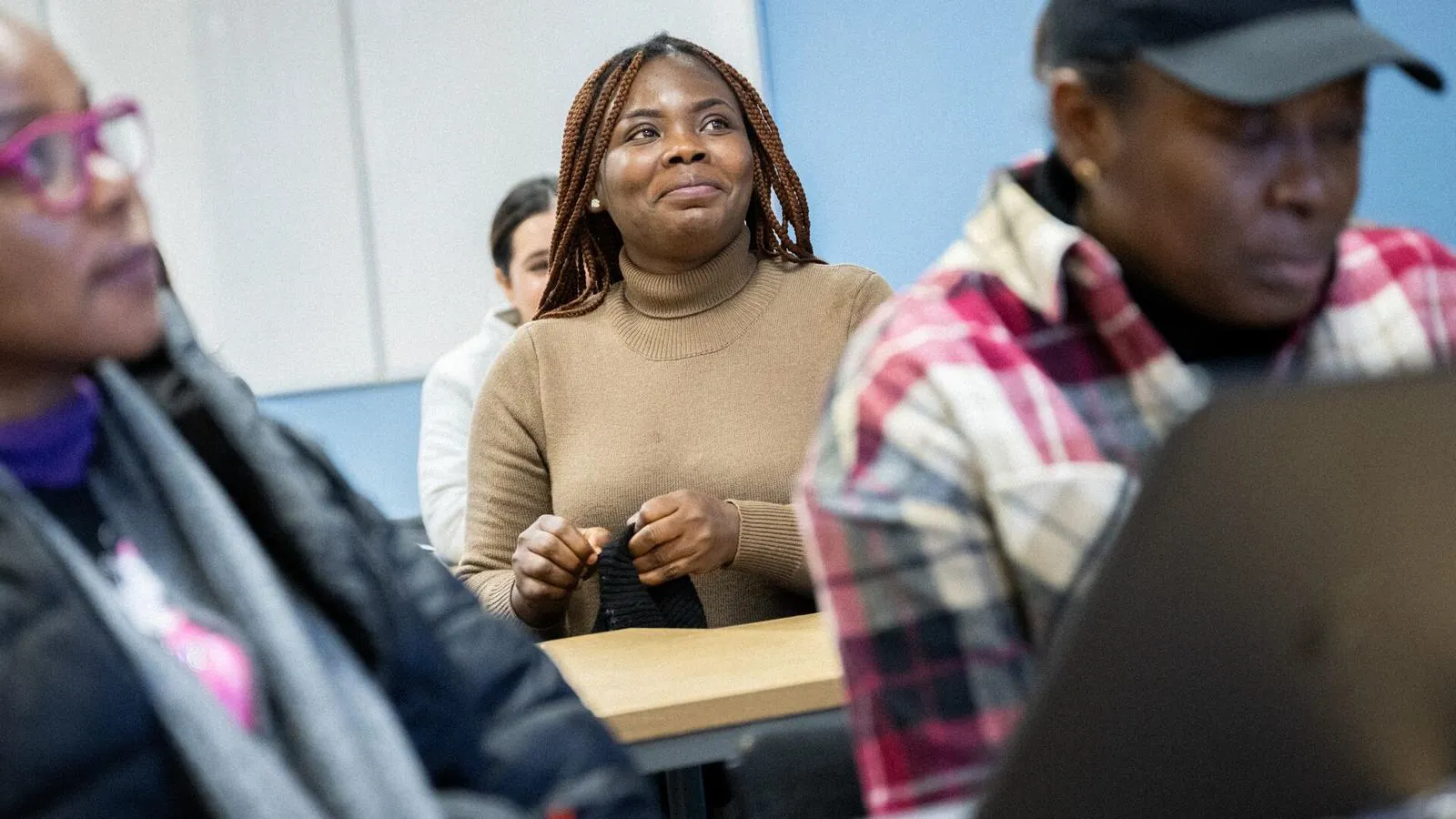 a female student in focus in a teaching room, with other students around her all learning together