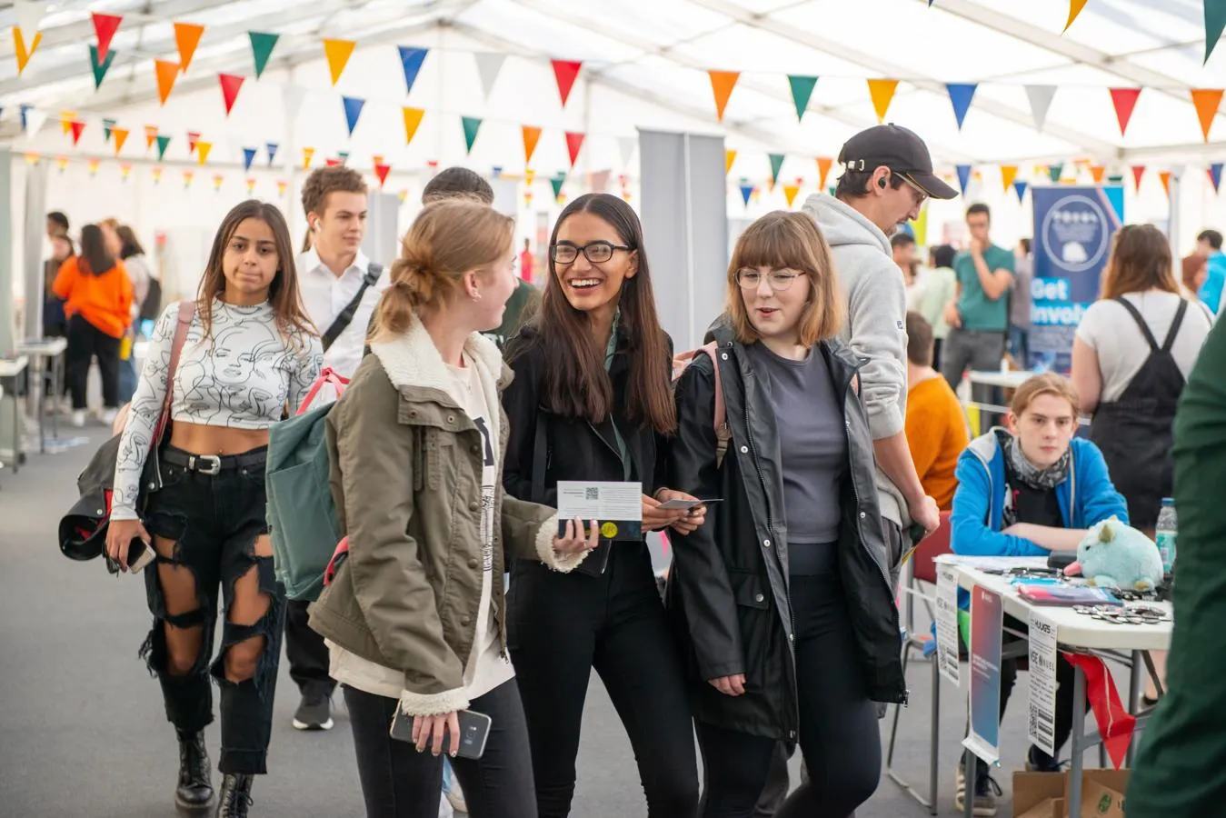 Three friends walk together through the Freshers Fair underneath colourful bunting