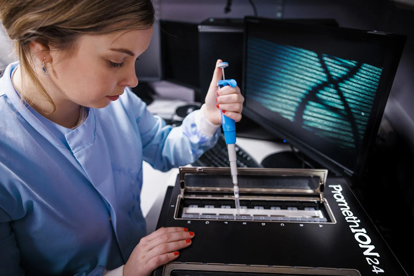 A woman in a blue lab coat uses a pipette in a laboratory