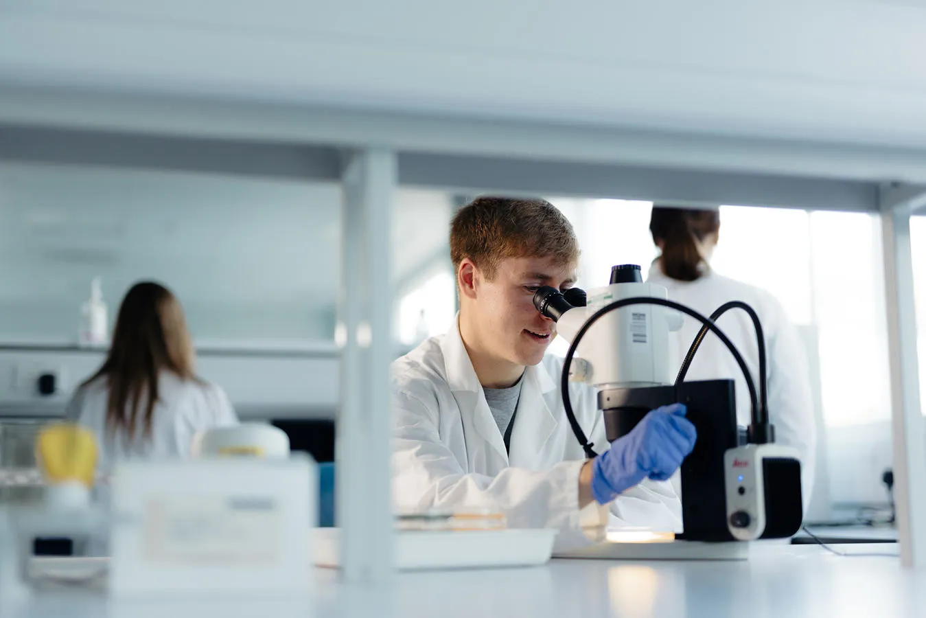 Student in lab coat using a microscope