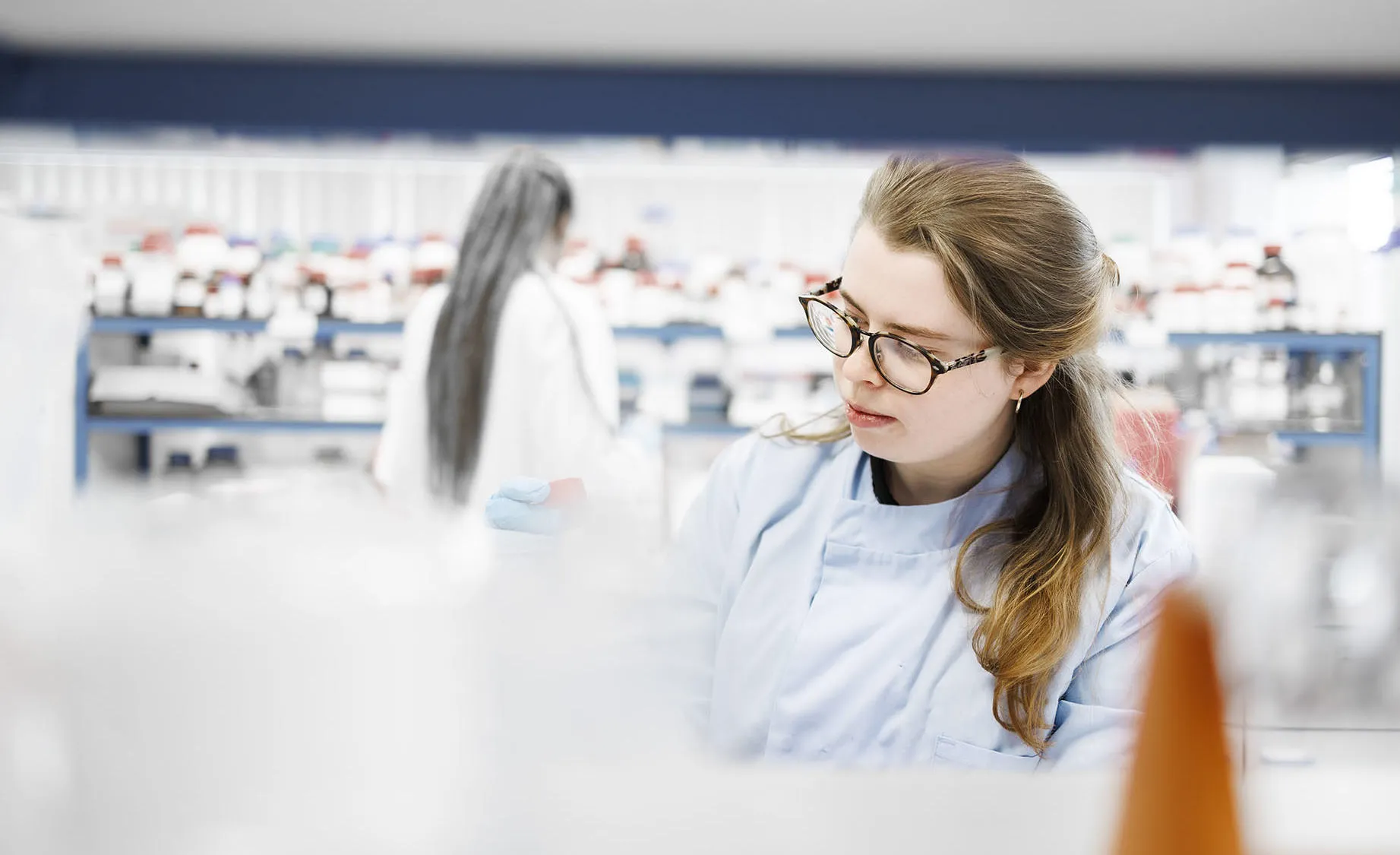 A woman in a lab coat observes something closely, indicating a scientific investigation in a lab environment.