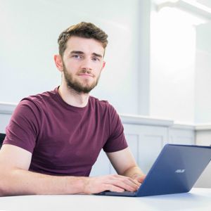 Student sat at desk posing in front of classroom