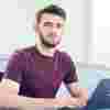 A young male student sat at a desk with a laptop looking directly the camera