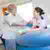 Two student midwives in white uniforms train with a dummy baby in a birthing pool