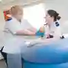 Two student midwives in white uniforms train with a dummy baby in a birthing pool