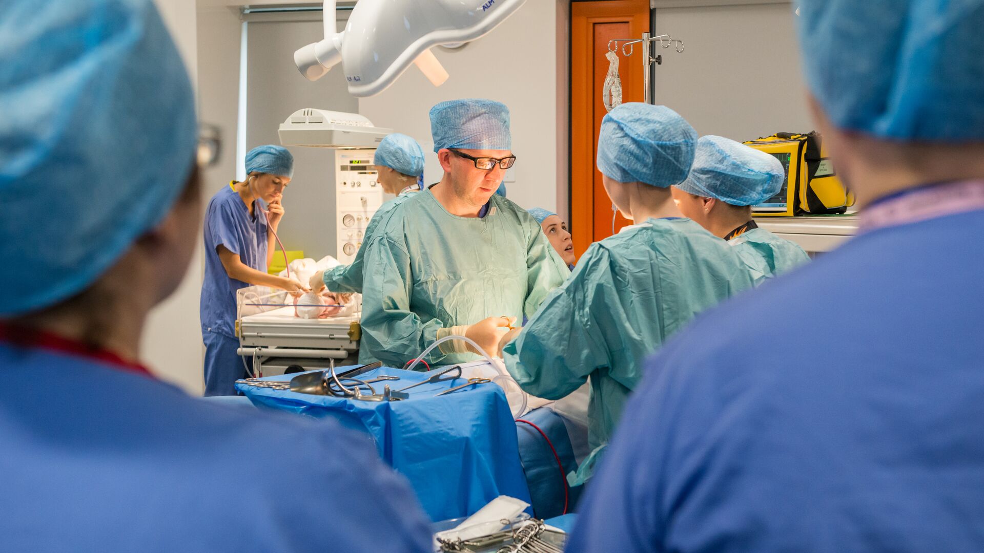 A surgeon in scrubs operates on a patient in a practical session in the operating theatre for students