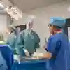 Female students wearing scrubs in a mock operating theatre with medical devices in front of them
