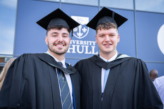 Two students stood smiling in their graduation cap and gown