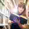 A Hull Philosophy student with an open book while browsing the bookshelves of the library.