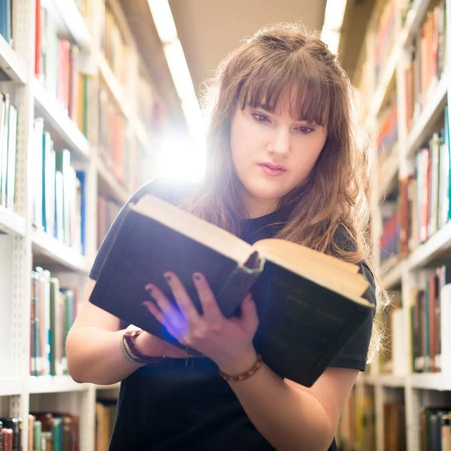 A Hull Philosophy student with an open book while browsing the bookshelves of the library.