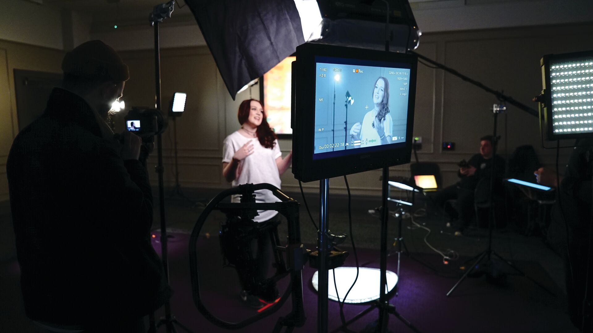 A young woman in a white t-shirt being filmed in a dark room with panelling on the walls