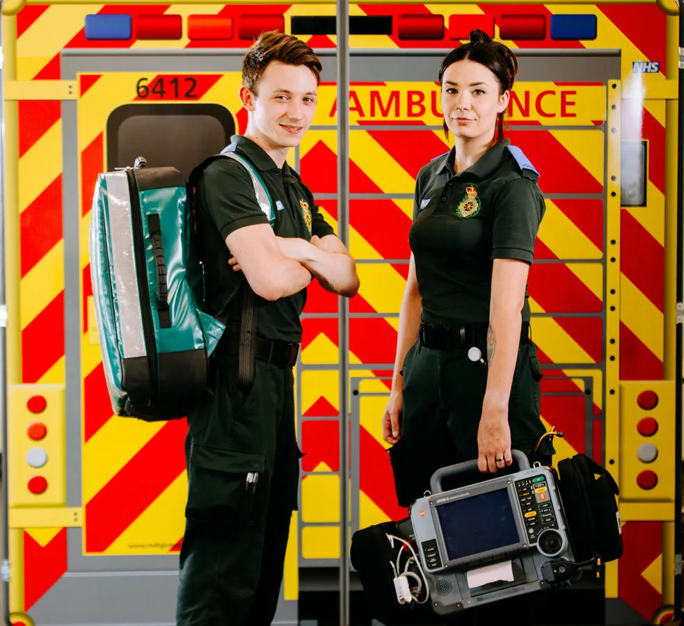 Two student paramedics stood in front of mock ambulance