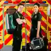 two male and female student paramedics stood in front of mock ambulance