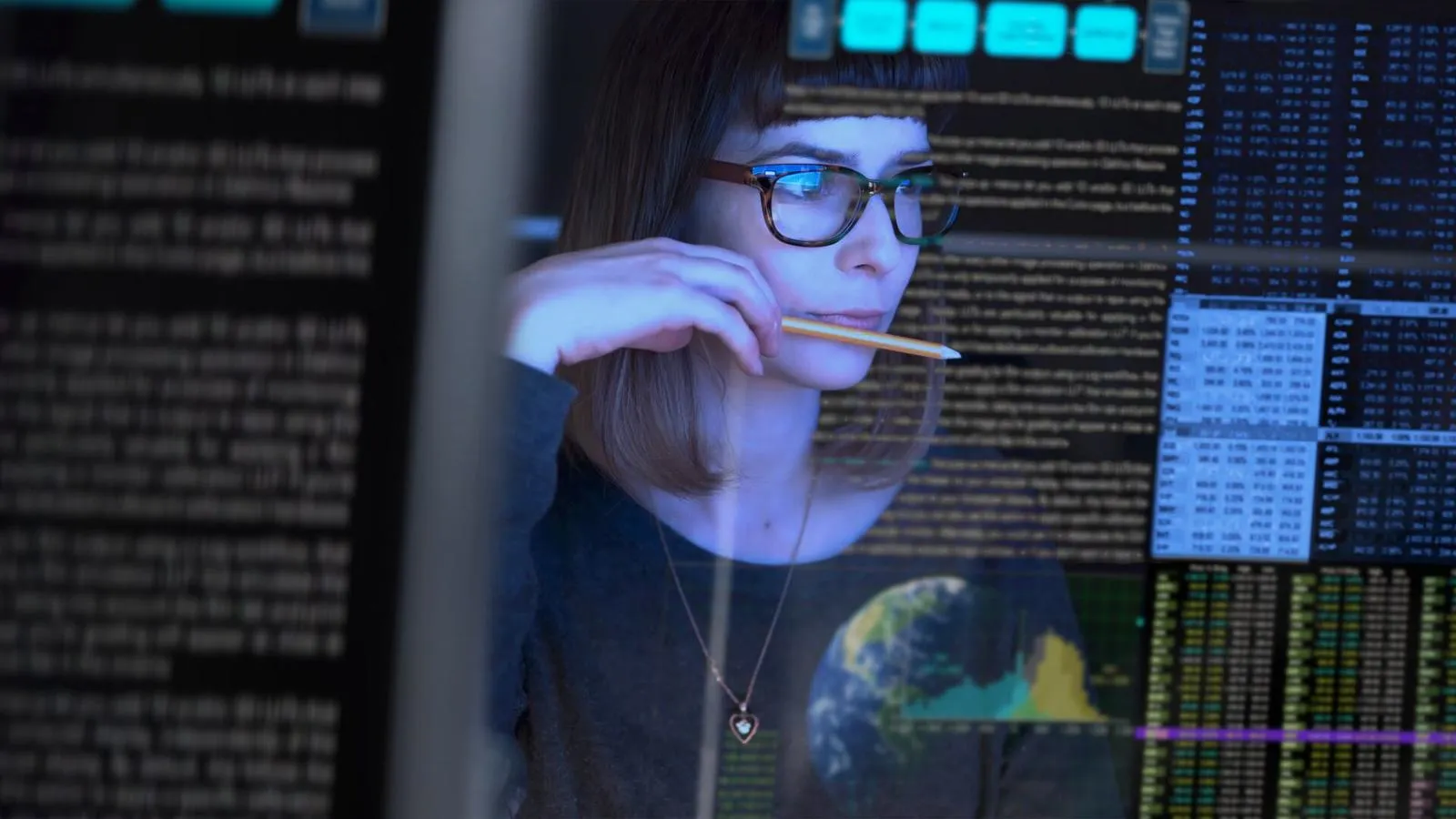 Female with glasses holding a pencil looking at data on computer