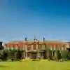 A large ivy- clad red-brick building with a bright blue sky and lawn to the front