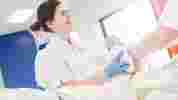 A smiling midwifery student in white NHS uniform practises cleaning a dummy baby after birth