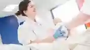 A smiling midwifery student in white NHS uniform practises cleaning a dummy baby after birth