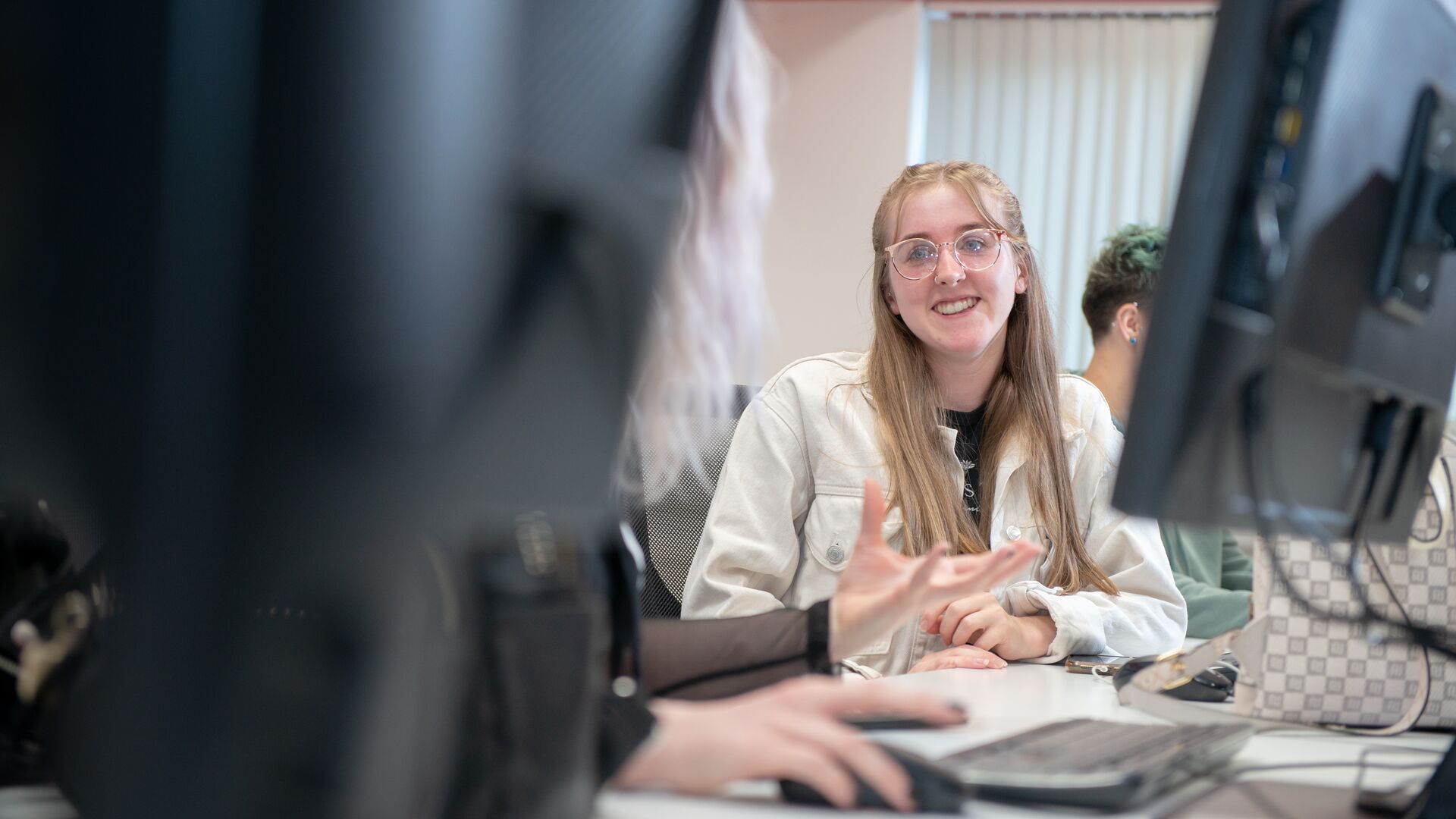 A student smiling at a friend whilst on the computer