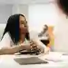 Female student sat at a table with her hands clasped over her notebook.