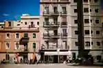 A row of cycles and scooters standing in front of an apartment building in Barcelona