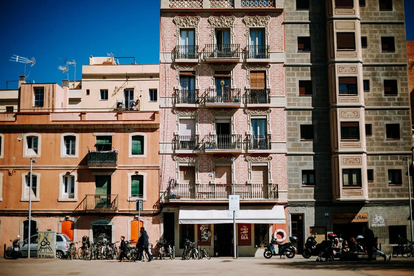 A row of cycles and scooters standing in front of an apartment building in Barcelona