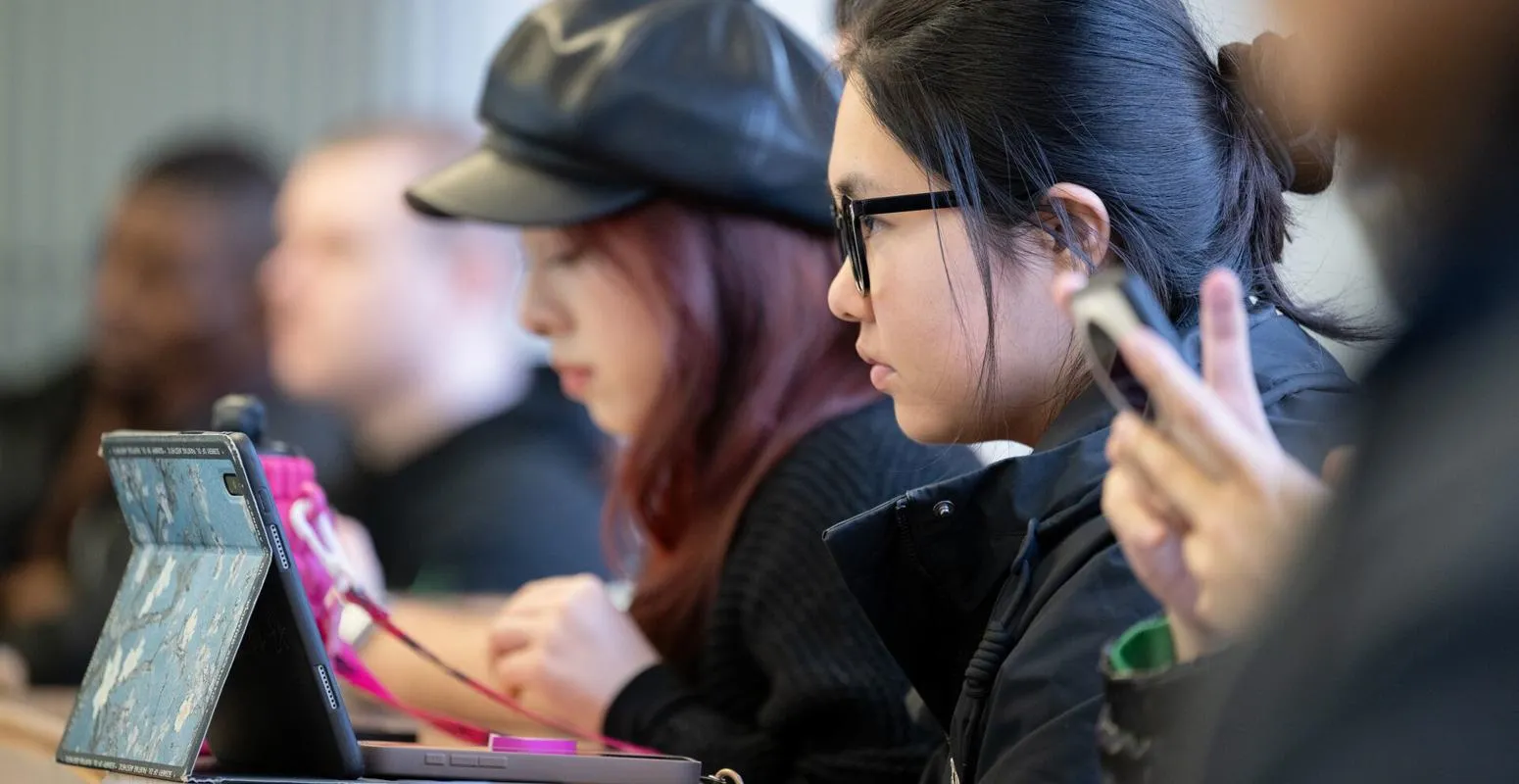 Two students sat at a desk on their phones
