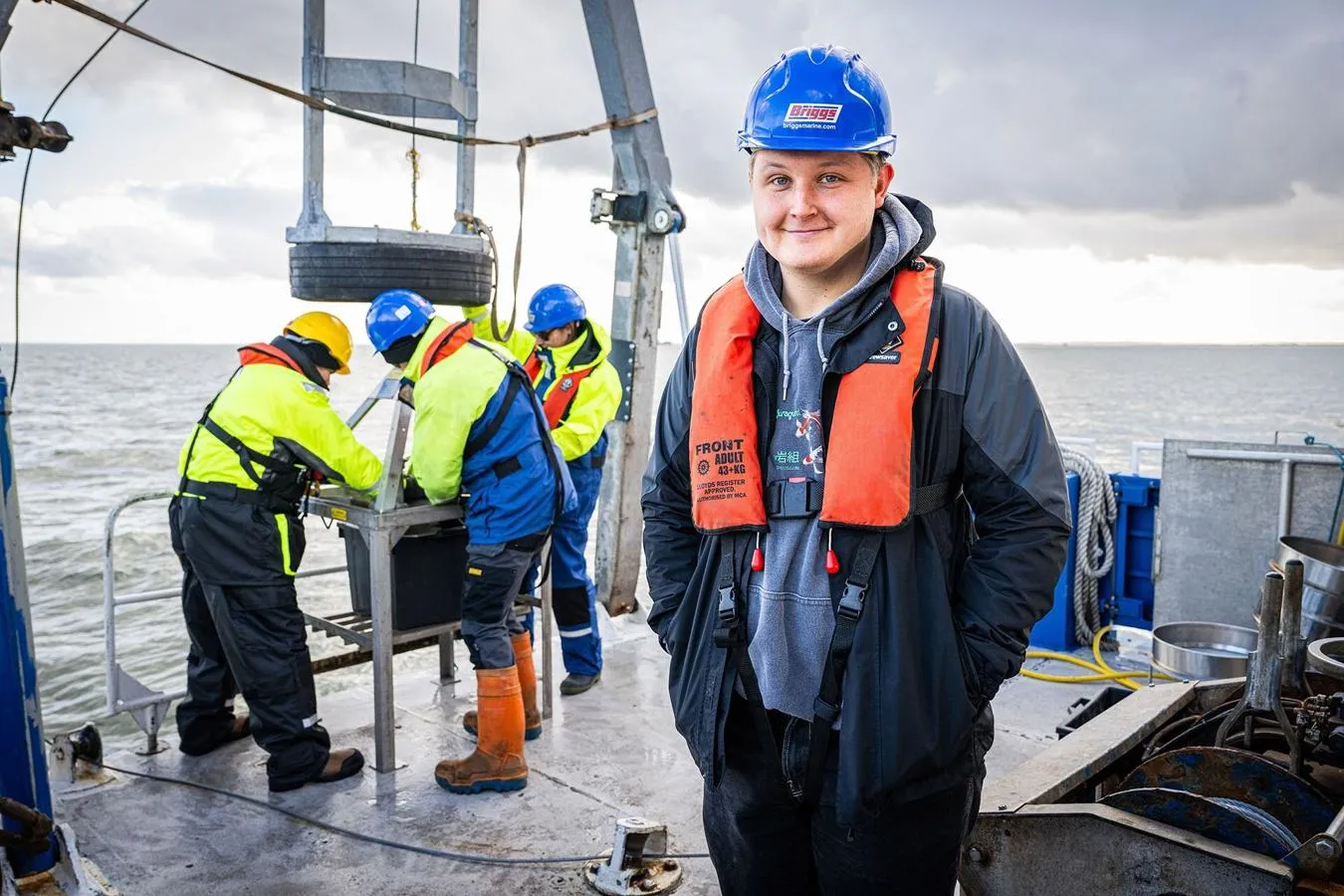 A marine biology student in an orange life vest standing on a boat out at sea